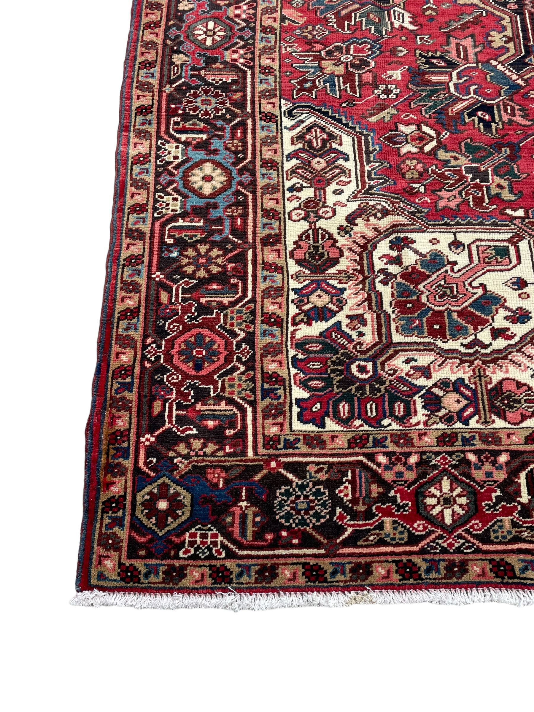 Persian Heriz red ground rug, central scrolled medallion on dark ground decorated with floral motifs, the surrounding field decorated with stylised plant motifs and smaller geometric symbols, guarded border with repeating pattern punctuated with rosettes and flower heads 