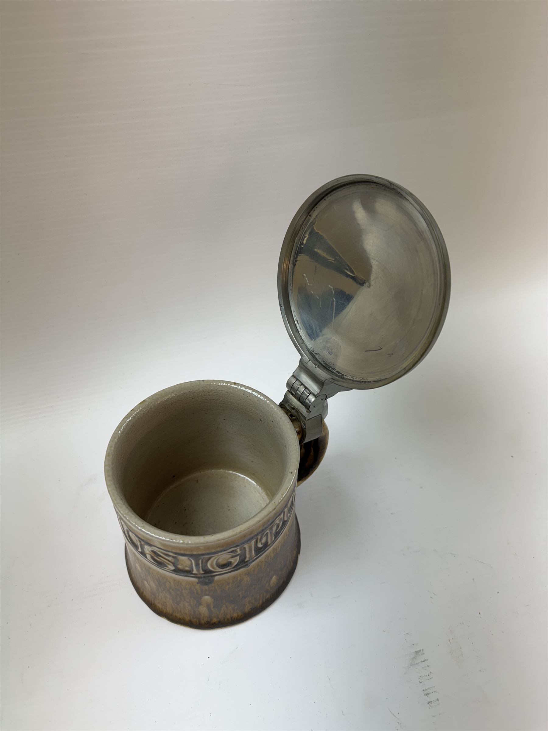 Arts and Crafts or Jugendstil tankard by Richard Riemerschmid, circa 1906, the cylindrical stoneware body reading 'Gaudeamus Igitur' (therefore let us rejoice), and finished in a brown glaze, with engraved slightly domed hinged lid, impressed mark beneath for Reinhold Merkelbach Grenzhausen, model number 2026 W, H14.5cm 