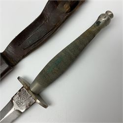 First Pattern Fairburn Sykes ''F-S'' Fighting Knife by Wilkinson Sword Ltd., the 17cm double edge steel blade with raised medial ridge to each side, each side of the ricasso with a recessed panel, one side with maker's name, the opposing side etched THE F~S FIGHTING KNIFE, with nickel plated brass recurving crossguard and diamond cut grip; in leather scabbard with metal chape