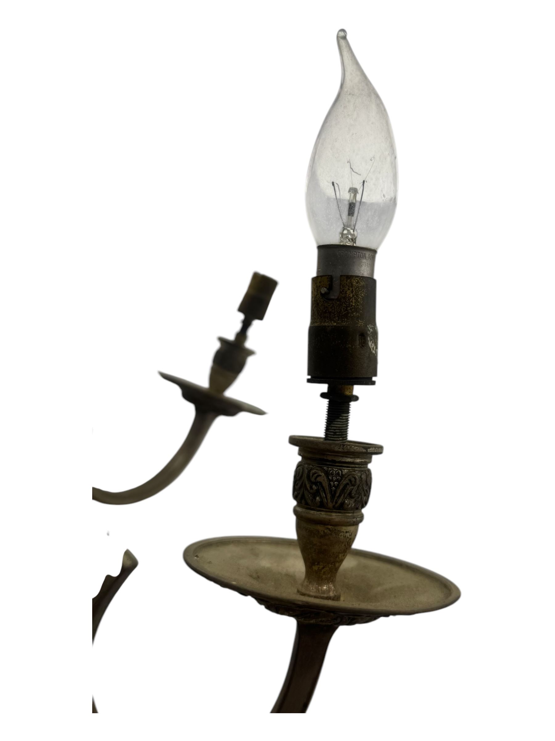 Pair of mid-20th century brass chandeliers, each with cast foliate and scroll decorated central body, issuing six scrolling arms with circular drip pans and bulb holders, suspended from integral ceiling loops