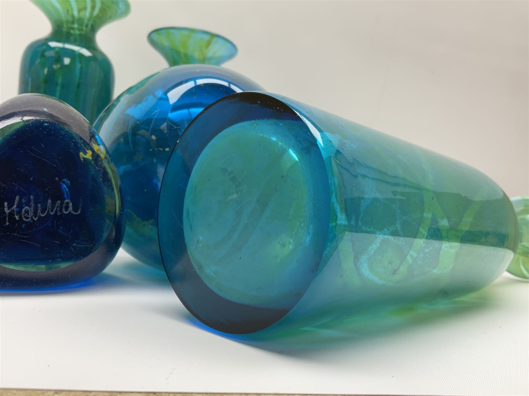 Quantity of M’dina art glass to include a streaked blue and green bottle form vase with captured bubble design and slender neck, H35cm, along with a paperweight, ovoid form vase and another vase all decorated in a blue, brown and white colour way, other contemporary glass examples etc with etched marks beneath