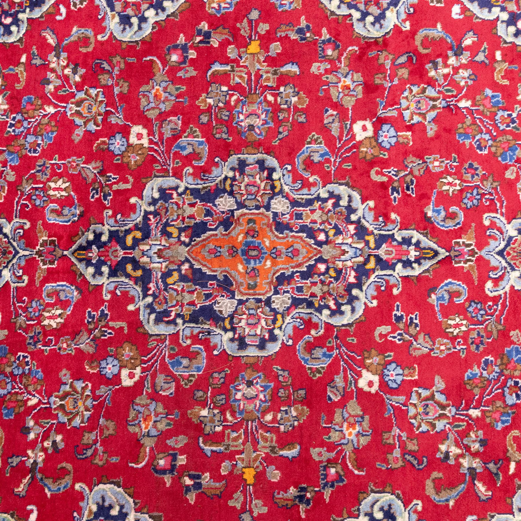 North East Persian Mesued hand-knotted carpet, deep red field with a finely drawn central elongated medallion of navy and ivory, issuing delicate scrolling vines, palmettes and floral sprays in a dense all-over composition, main border on dark ground decorated with a continuous palmette and vine scroll, flanked by multiple narrow guard stripes incorporating rosettes and stylized floral devices, with cotton fringe ends 