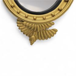 Early 20th-century Regency-style giltwood convex mirror, circular plate within a ball-mounted frame surmounted by an eagle cresting and flanked with scrolls, apron carved with foliate decoration 