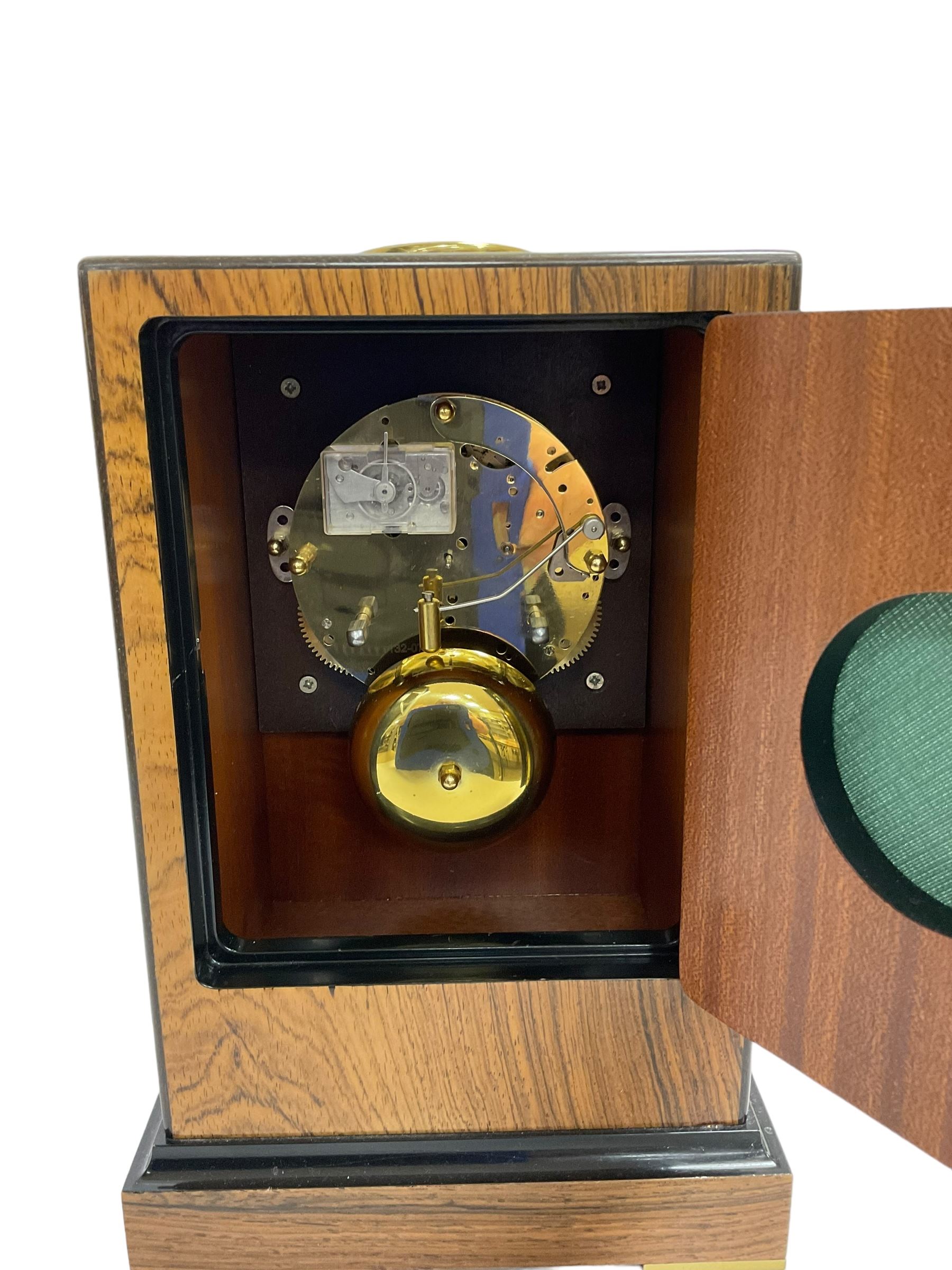Knight & Gibbins London - 20th century 8-day marquetry inlaid mantle clock in rectangular case on a short plinth, glazed circular dial with Roman numerals and steel moon hands, two train striking movement with a floating balance escapement striking the hours and half hours on a bell, rear set and wound. With key.   
