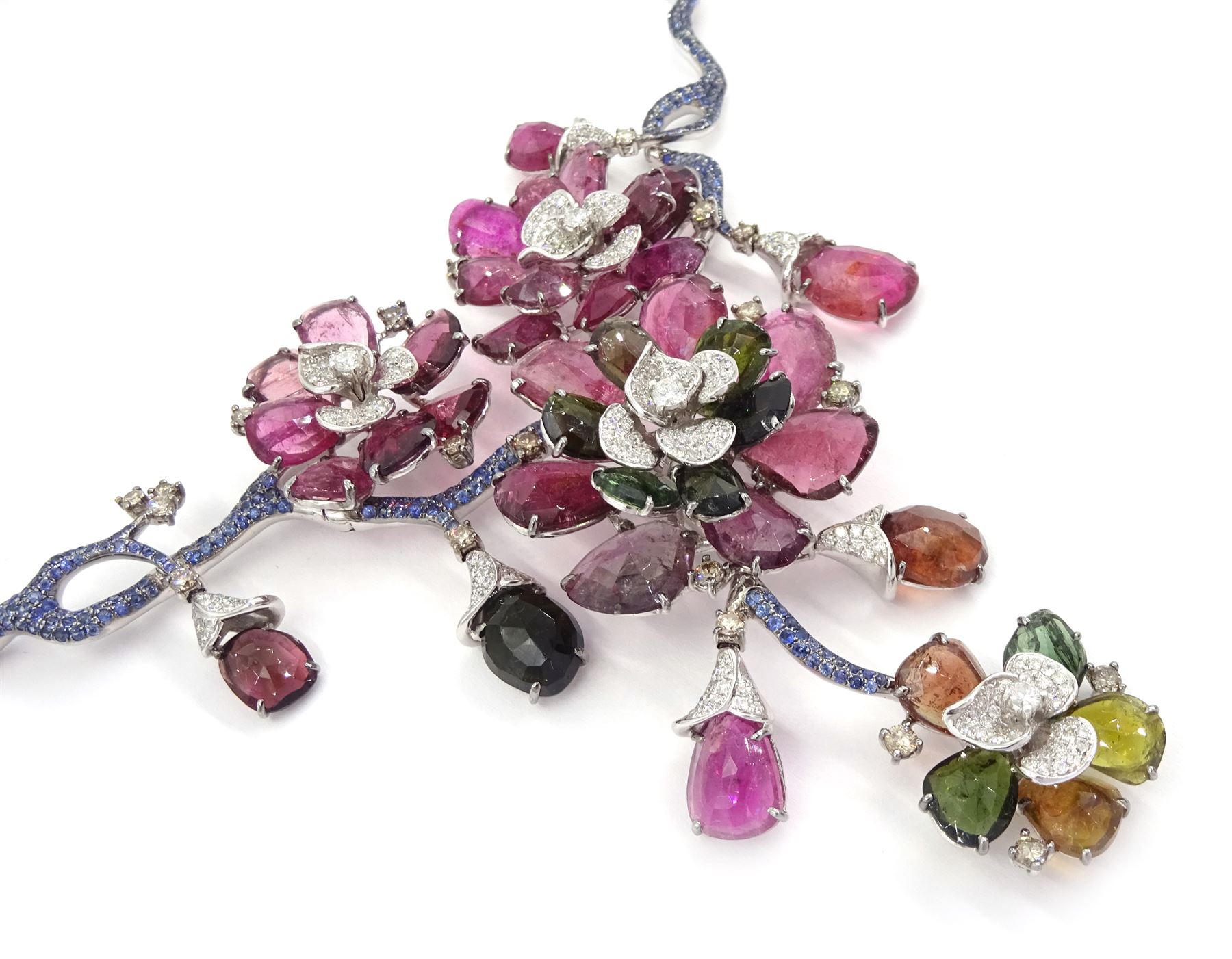 18ct white gold gemstone set floral jewellery suite, comprising necklace, pair of earrings and bracelet, each with tourmaline flower petals, round brilliant cut diamond centres and sapphire stems, stamped