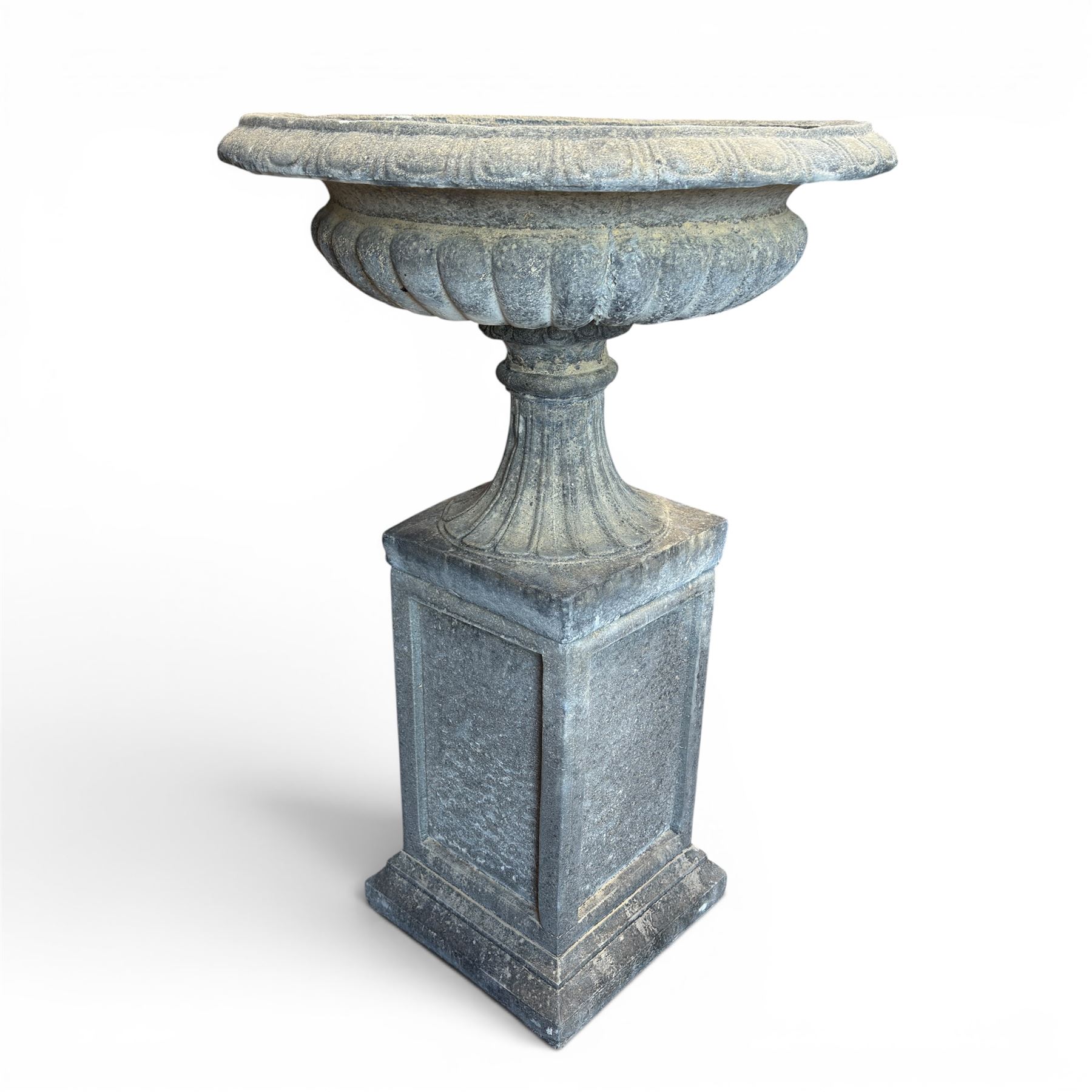 Pair of cast stone garden urns of kylix form on pedestals, the broad egg-and-dart moulded rim over a shallow gadrooned underbelly, with waisted tapering base, raised on matching plinth bases with faux panelled facia