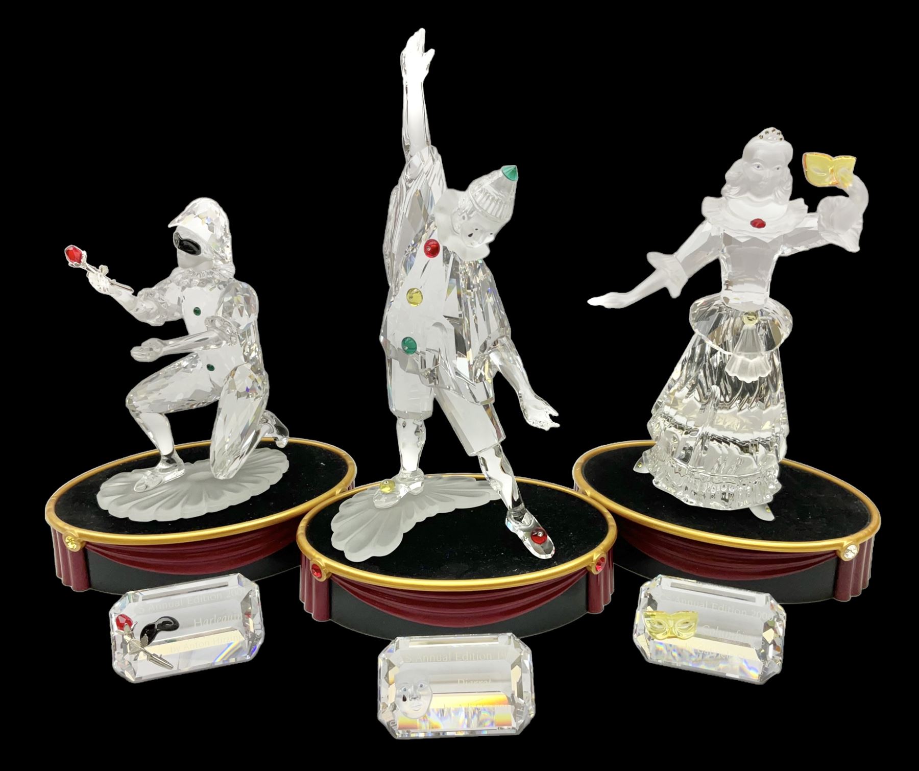 Swarovski Crystal Masquerade trilogy; 1999 Masquerade Pierrot, 2000 Columbine, 2001 Harlequin all with accompanying plaque, stand and original box, together with a glass display case with mirrored back and sides 