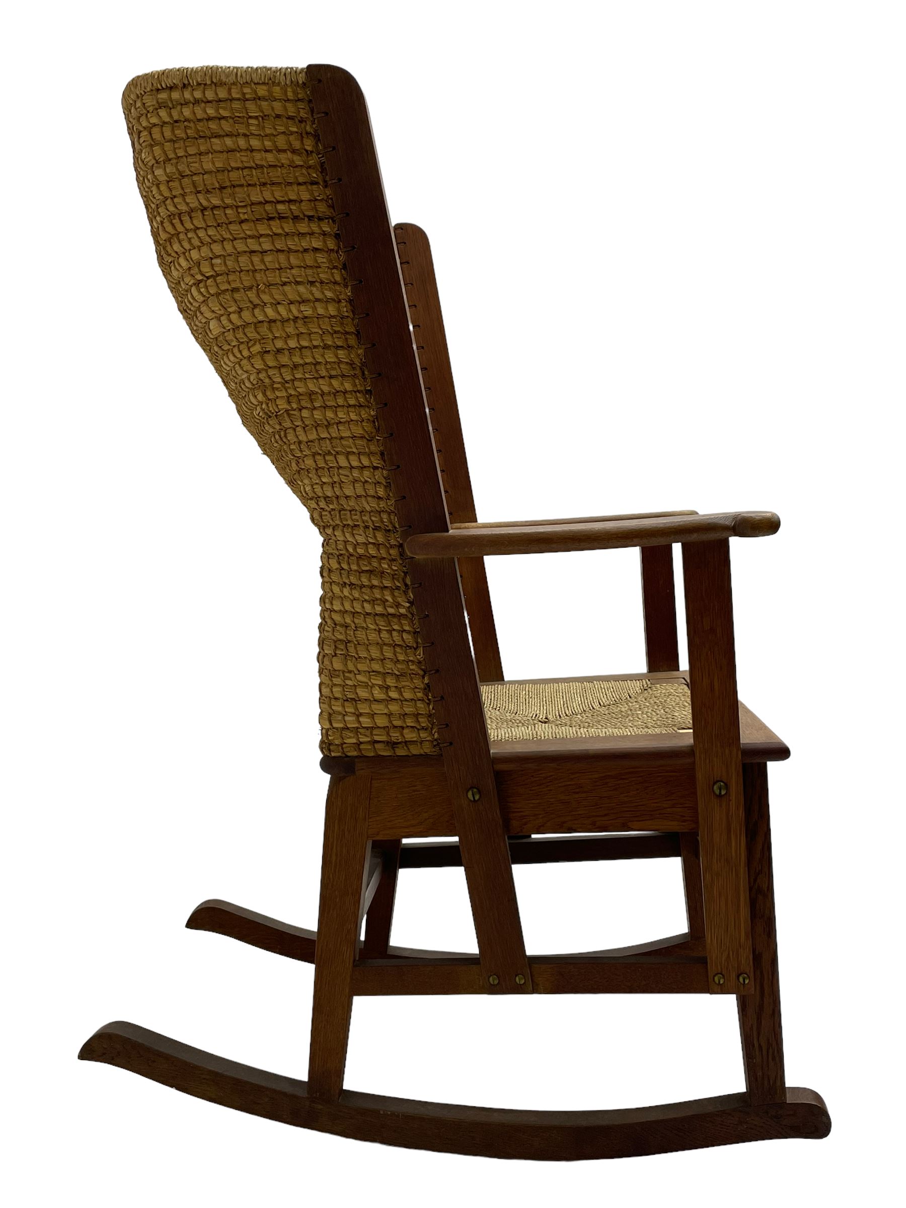 Reynold Eunson (1932–1978) for David Munro Kirkness, Kirkwall, Orkney - oak framed Orkney rocking chair, woven straw curved back, drop-in rush seat, the arm terminals with carved end scroll, on square tapering supports joined by plain stretchers, the front rail inscribed with makers marks
