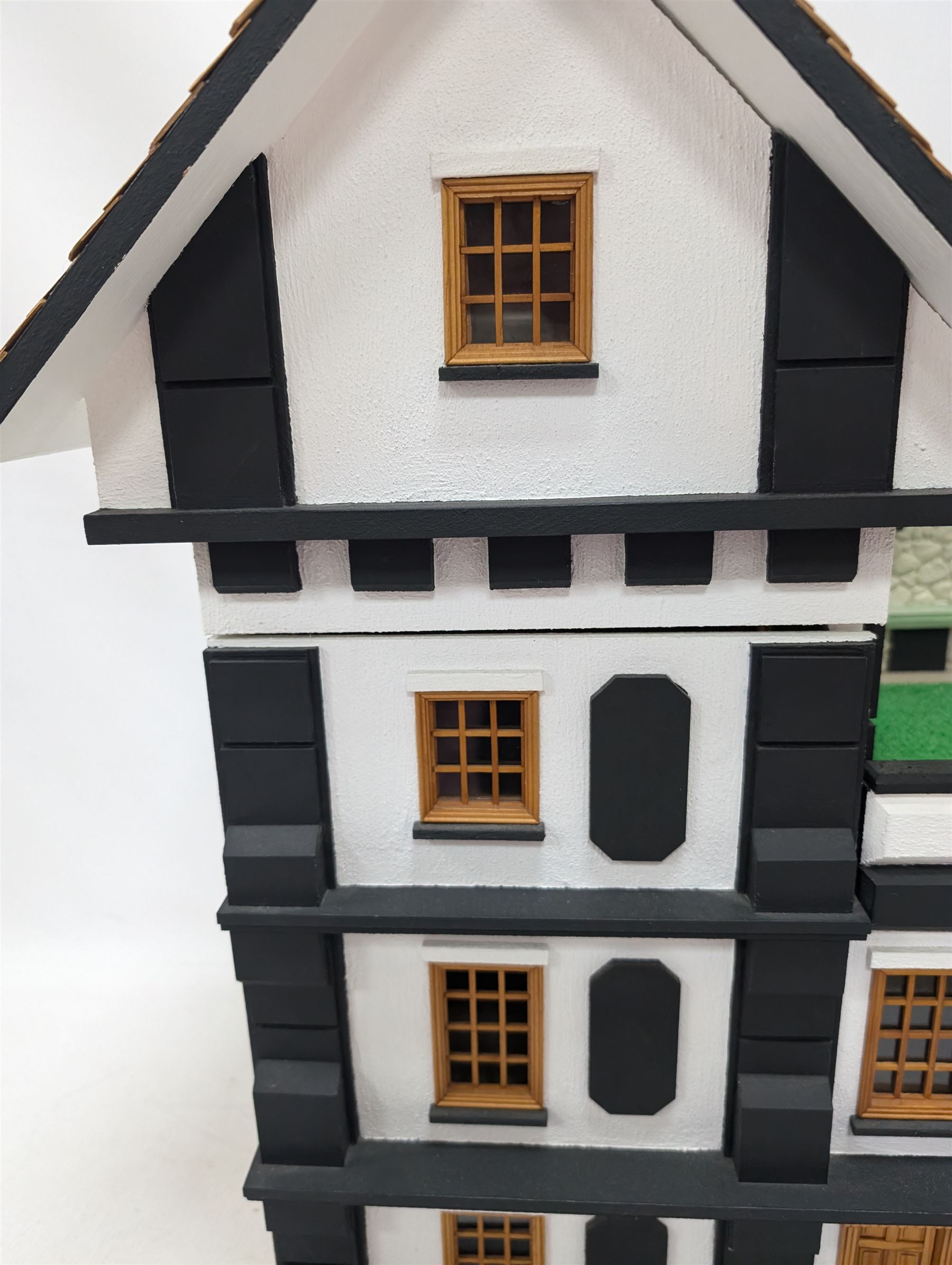 1:24 scale four-storey tudor-style dolls house, with black and white exterior, balcony garden, glazed panelled windows and wooden shingle roof, with decorated interior and wired fireplaces and lighting, H65cm, W58cm, D31cm, 