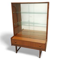 Turnidge of London mid-century teak display cabinet, rectangular top with a pair of glass sliding doors enclosing two adjustable shelves with mirrored back, projecting lower section incorporating one full-width drawer with recessed circular handles, raised on square-section legs with lateral stretchers  