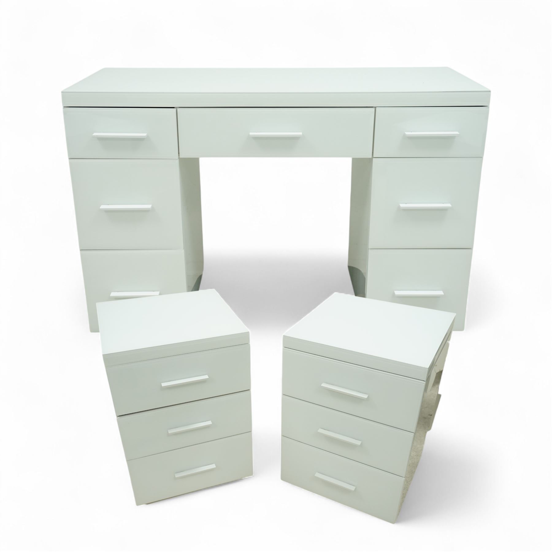 Contemporary white and glass twin pedestal dressing table and two matching bedside chests, dressing table with rectangular top above seven flush-front drawers arranged around a central kneehole, with white matching pulls, bedside chests each with square top over three drawers with integrated handles, plain sides and plinth bases

Bedside tables (W 121cm D 41cm H 82cm)
Dressing table (W 45cm D 45cm H 66cm)