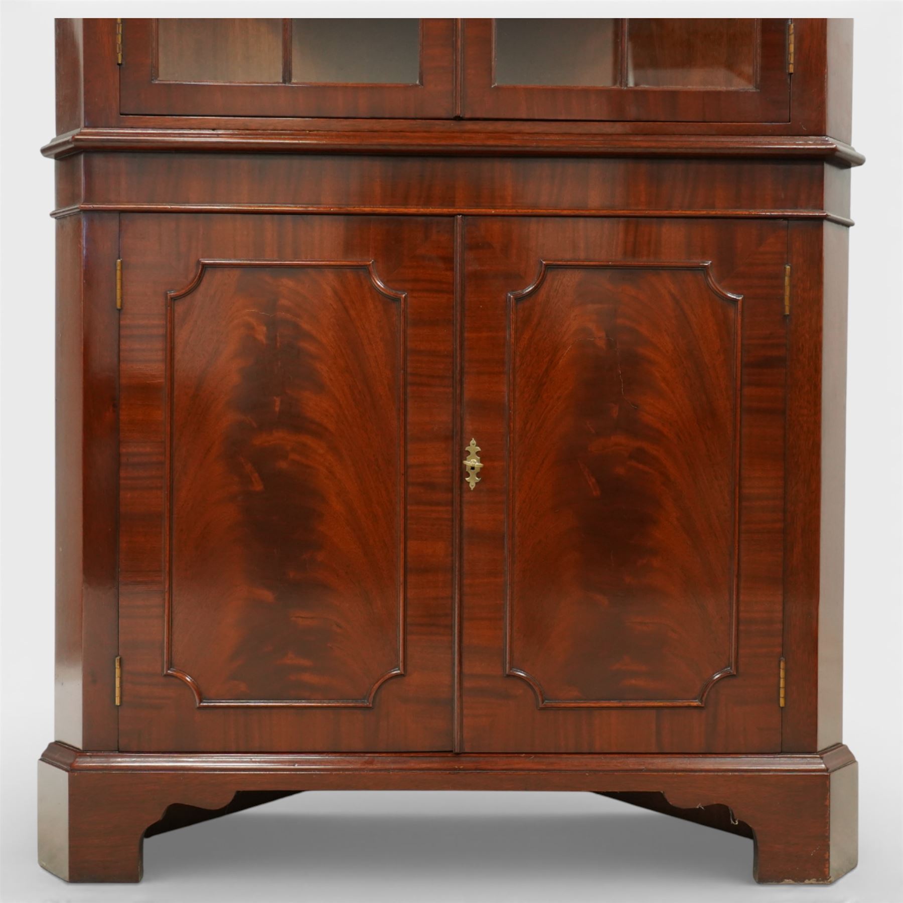 William Tillman - Early 20th century mahogany corner cabinet, the projecting moulded cornice with dentil detail over a glazed upper section enclosed by a pair of astragal glazed doors with Gothic arched tracery, the interior fitted with shaped shelves, above a moulded waist and a lower cupboard enclosed by two panelled doors with shaped fielded panels, raised on bracket feet