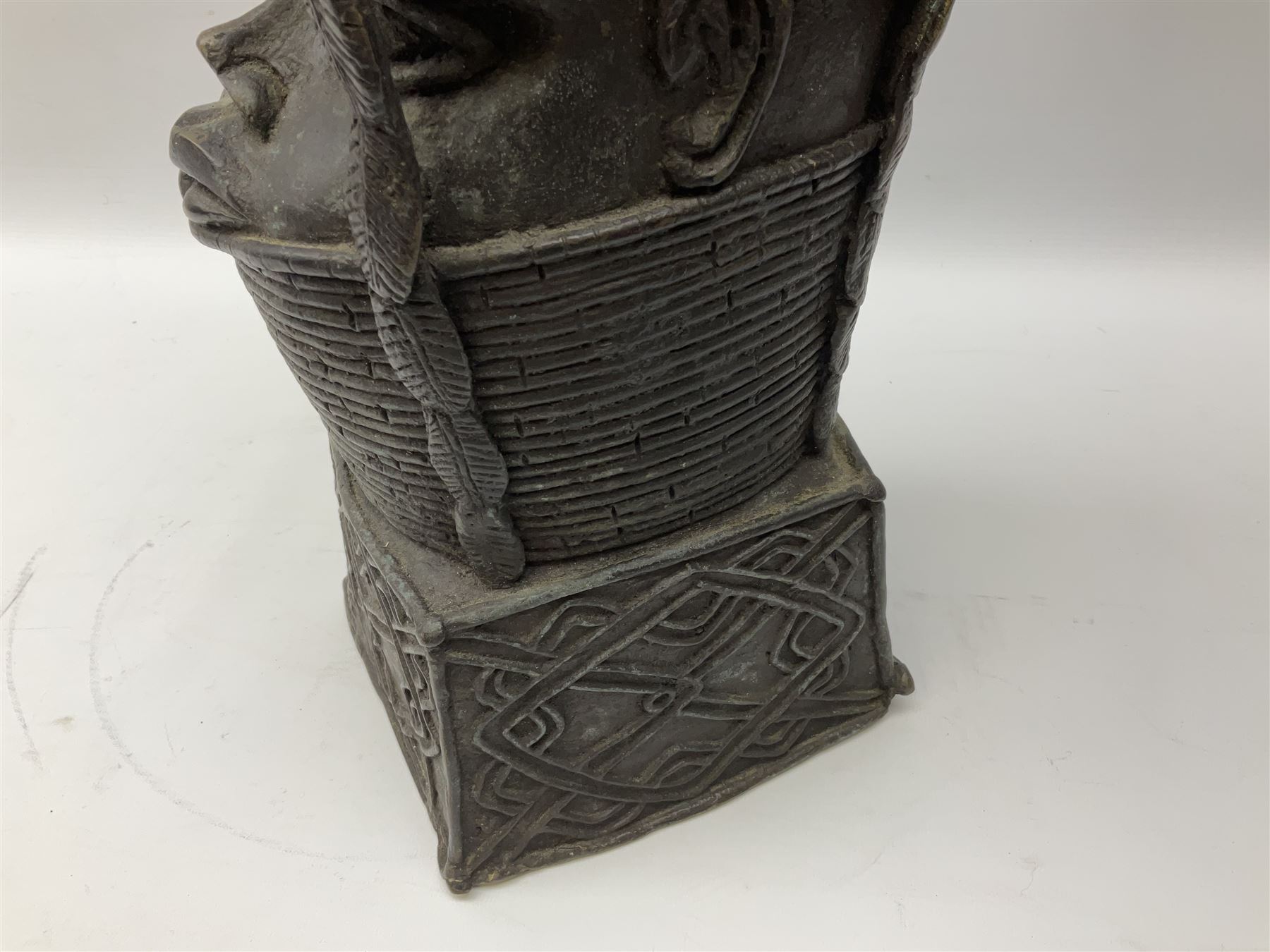 20th century Benin bronze head of an Oba, donning headdress and neck rings with wide open eyes, raised upon a tapering square base, the sides with relief cast knot decoration, H39cm