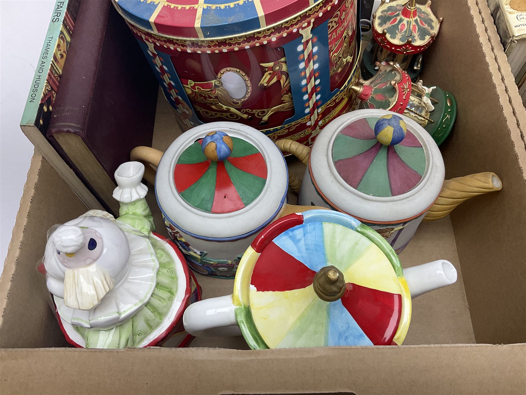 Collection of circus and fairground collectables, to include teapots, biscuit tins, including musical examples, and four Circus/fair themed books, including two library first editions