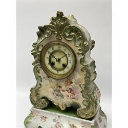An early 20th century French porcelain clock with rococo scrolling in a cartouche form with gilt highlights, adorned with applied transfer images of cupid, cherubs and a sleeping maiden, matching porcelain plinth, eight-day two train Parisian movement striking the hours and half-hours on a bell, countwheel movement with a recoil escapement, enamel dial with a recessed centre, gilt winding collets, upright Arabic numerals and minute markers, steel fleur de Lis hands, cast brass bezel with bevelled glass.
With pendulum and Key.   
