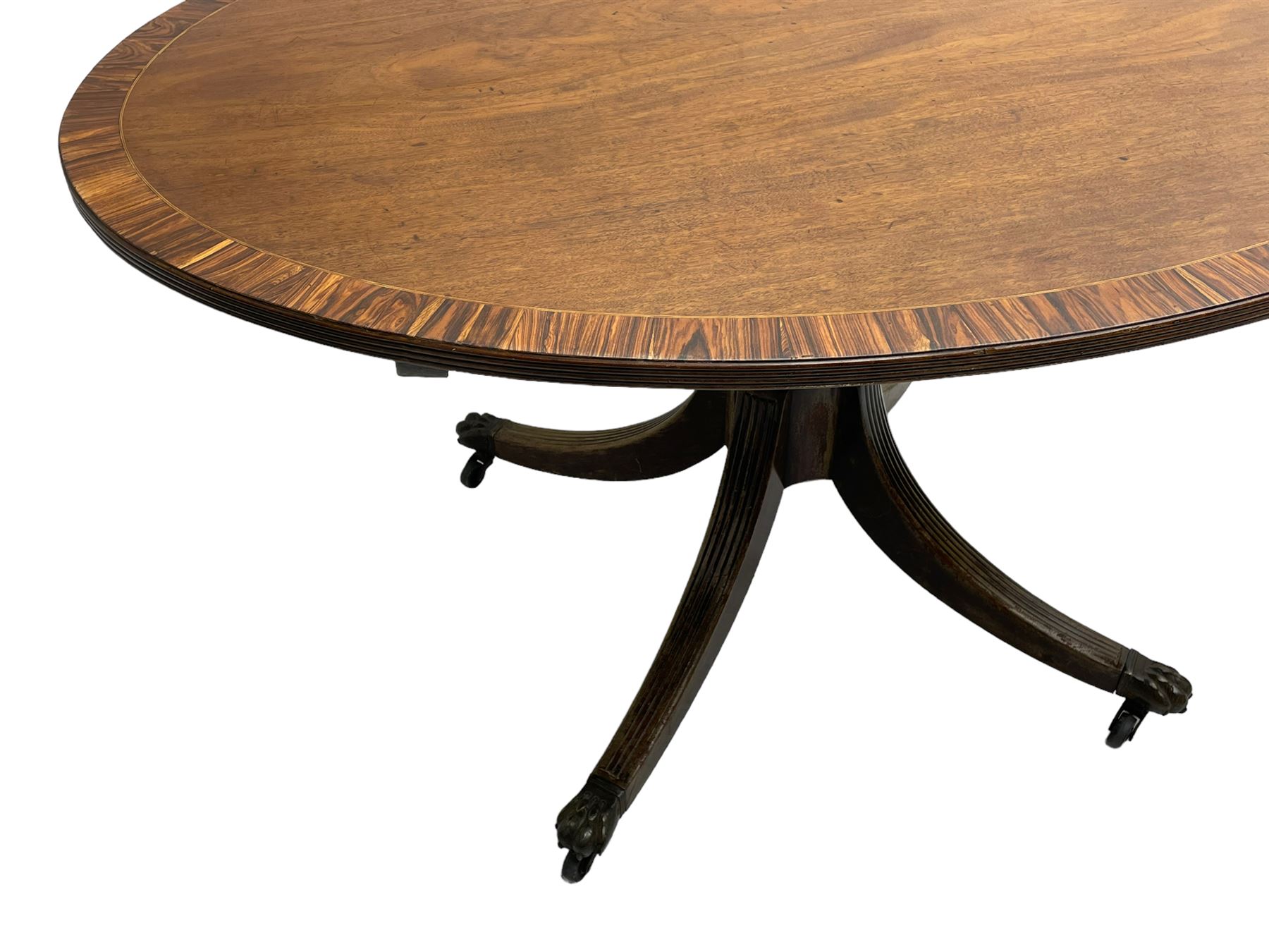 George III mahogany breakfast table, the oval top with a kingwood band and boxwood stringing, raised on a turned vasiform pedestal terminating in a fluted sabre tripod base with hairy paw feet and castors