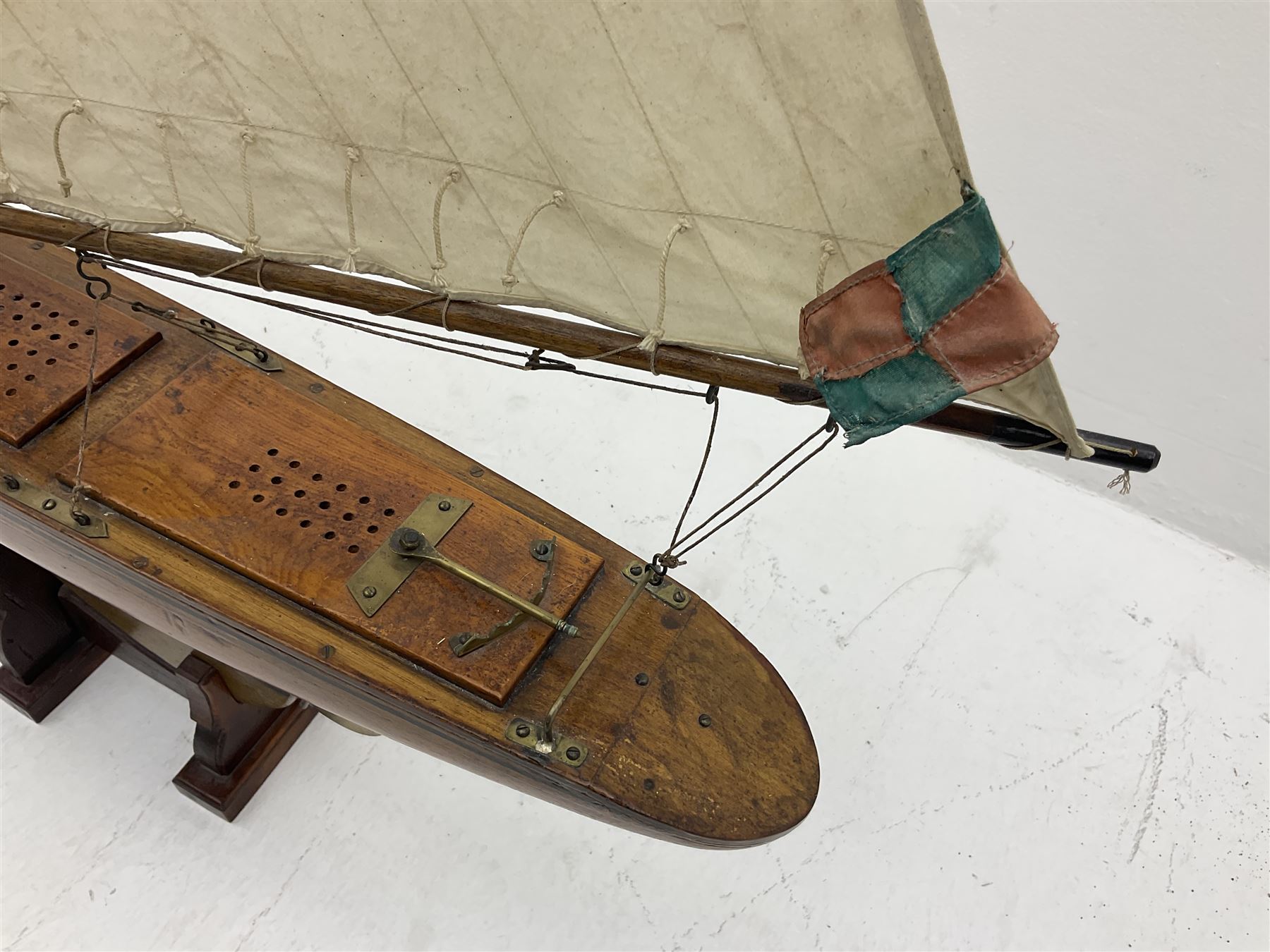 Early 20th century large pond yacht with mahogany hull, stained pine keel with brass rudder, simulated deck hatches and brass fittings, rigged as a staysail schooner (?) with four sails L117cm H148cm; loose mounted on stained pine stand