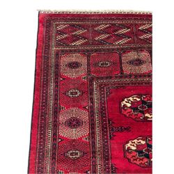 Afghan Bokhara red ground carpet, the field decorated with four rows of Gul motifs interspersed with Hac motifs, the border with lattice pattern panels within small geometric guard stripes, geometric patterned end panels