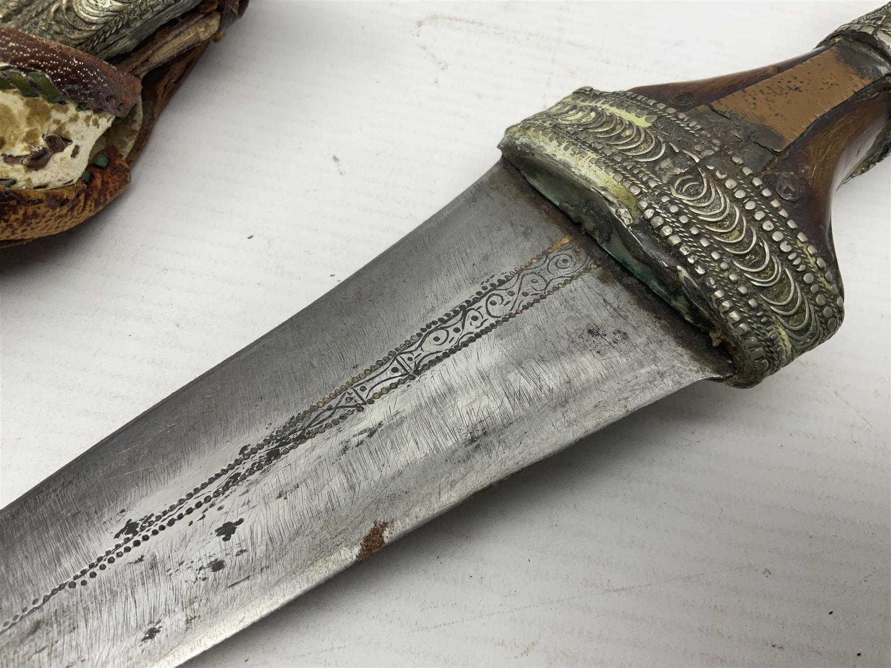 Saudi Arabian khanjar dagger with 29.5cm curving double edged  steel blade; white metal and copper mounted horn grip; in white metal mounted brass and leather scabbard incorporating embroidered leather wearing strap