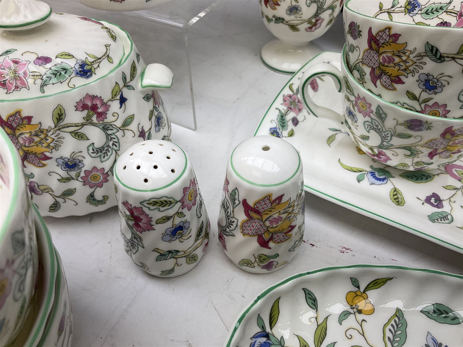 Minton Haddon Hall pattern tea and dinner wares, including basket dish, two covered tureens, six dinner plates, eight dessert plates, twelve tea plates, six soup bowls, six cereal bowls, teapot, coffee pot, milk jug, covered sucrier twelve tea cups and saucers, six mugs, footed bon bon dish, pair of candlestick holders, cake knife and slice etc (81)