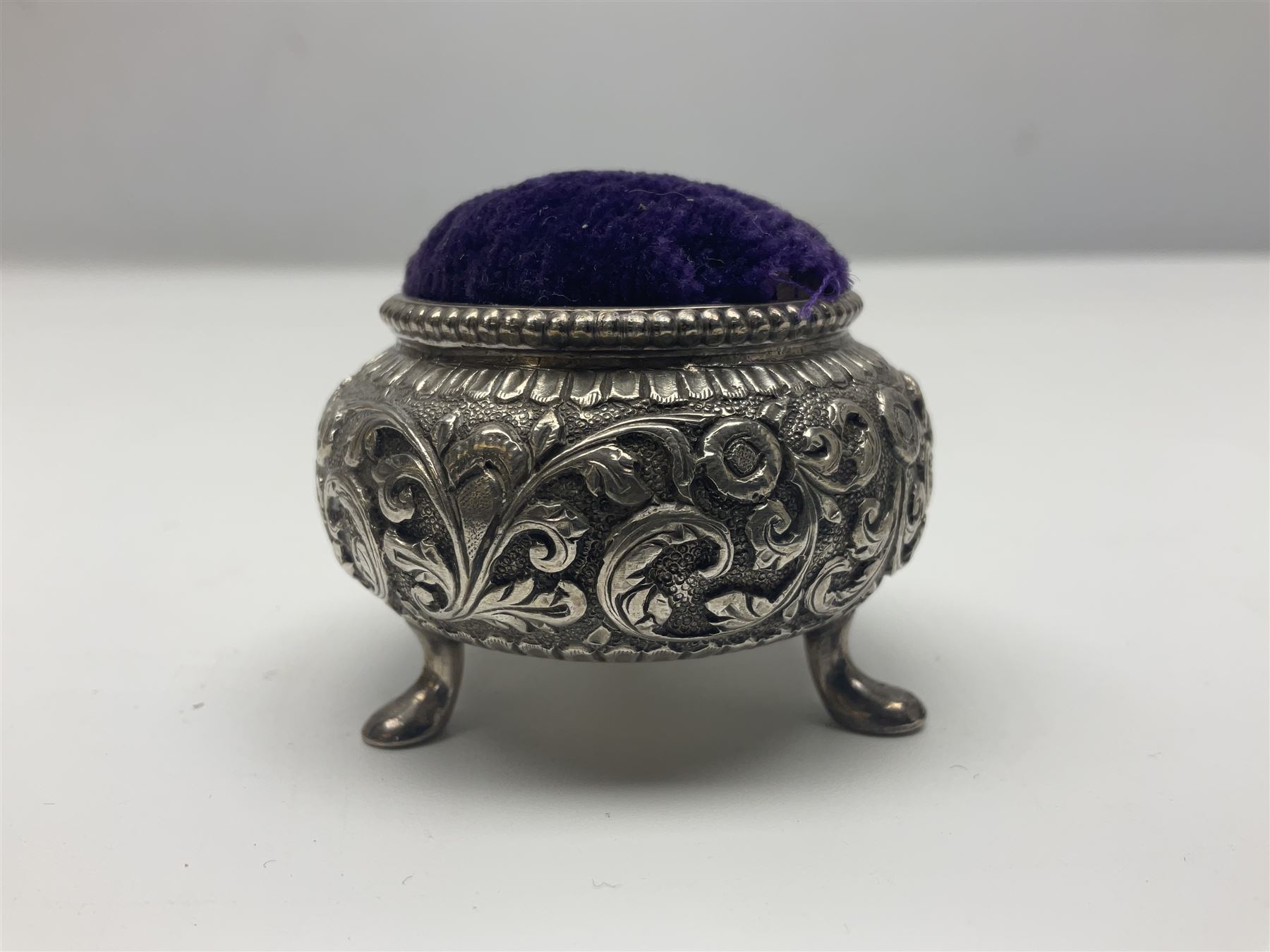 Three pin cushions, comprising gilt metal pig, silver plate shoe, circular pin cushion on threel feet, together with black pin holder with silver writing to the lid 