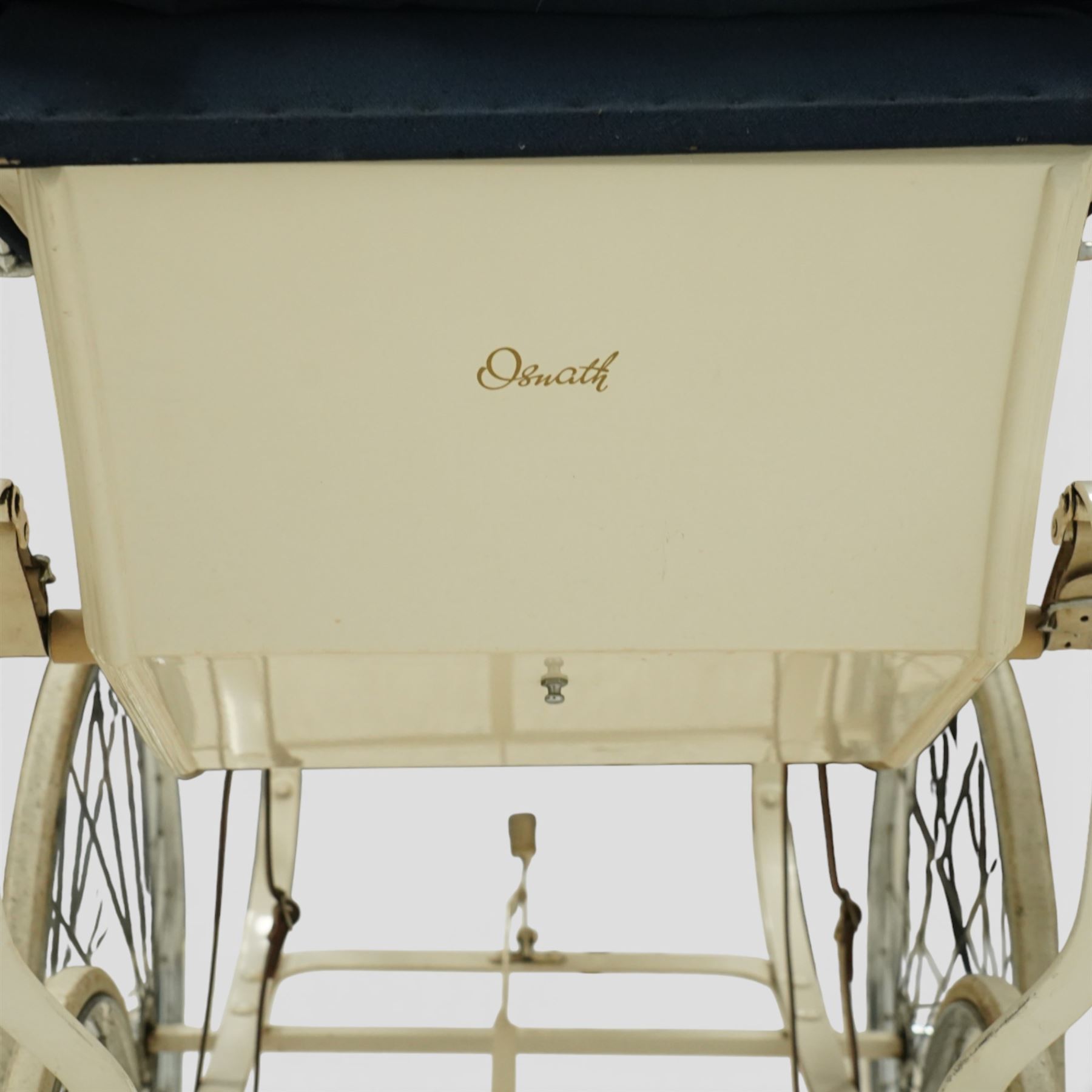 Mid-20th century Osnath pram, the cream painted metal body with navy fabric hood and apron, cream vinyl lined interior fitted with patterned mattress, raised on sprung metal supports with spoked wheels and white rubber tyres