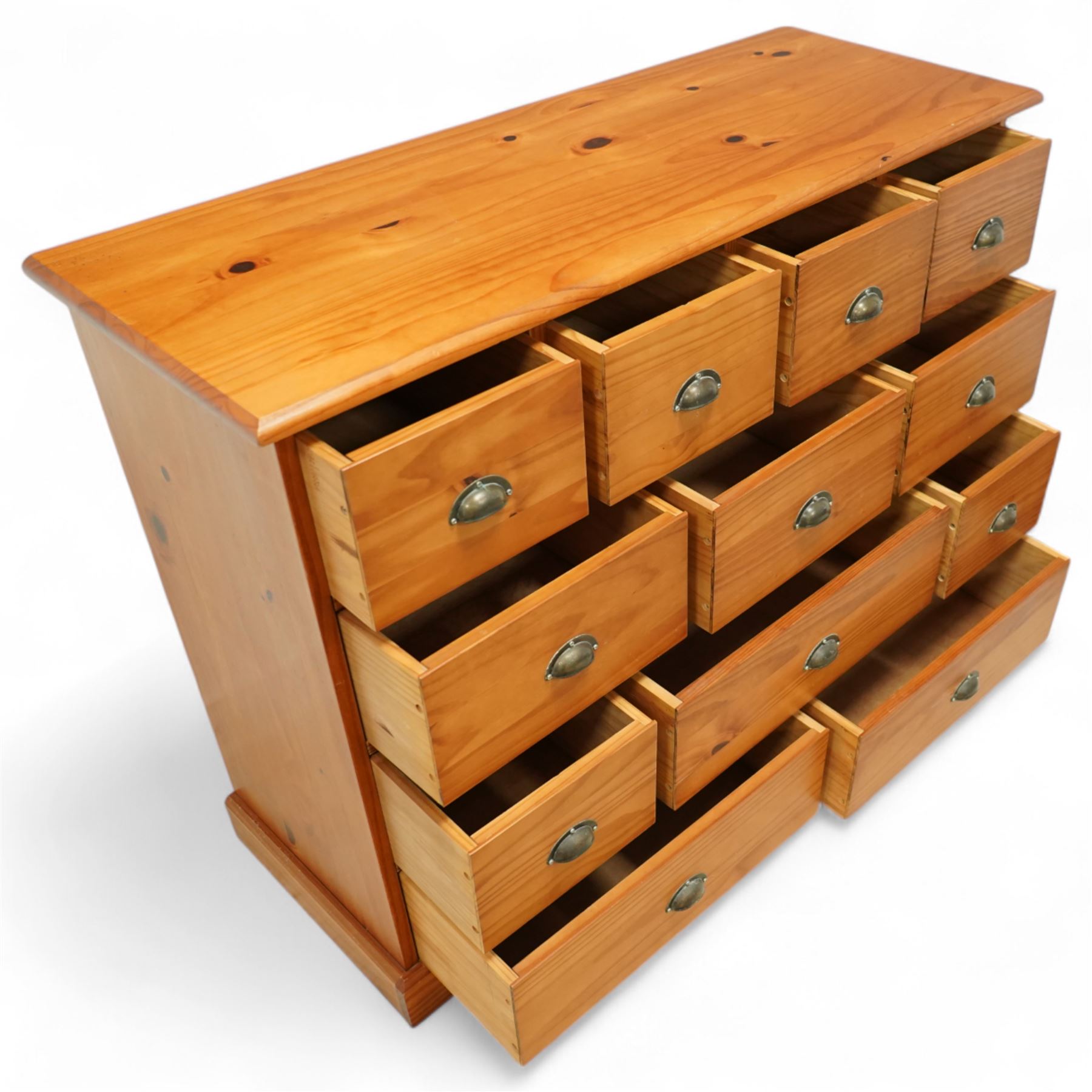 Late 20th century pine merchants chest, rectangular top over an arrangement of twelve small and four larger drawers, each with recessed panel facias and brass cup handles, plinth base