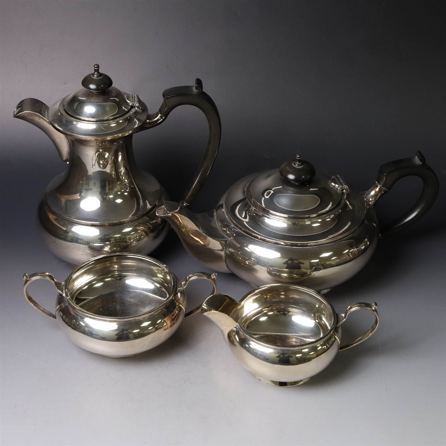 Mid 20th century silver four piece tea service, comprising teapot, hot water pot, open sucrier and milk jug, all of squat bellied form, the teapot and hot water pot with ebonised handles and finials, hallmarked Walker & Hall, Sheffield 1953, hot water pot H19cm