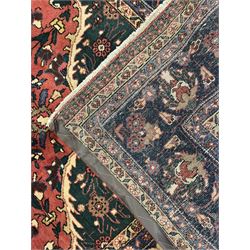 North East Persian Meshed crimson ground carpet, central indigo and green medallion with floral decoration, busy field with trailing foliage and stylised flowers, matching spandrels with floral motifs, indigo border featuring scrolling vines and palmettes, framed by narrow floral guard bands