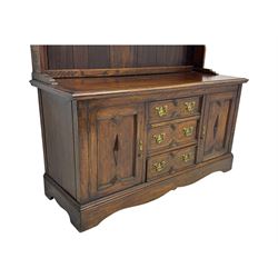 Late 19th century oak dresser, the upper section with two shelves beneath a shaped cornice, the lower section with a central bank of three drawers flanked by cupboard doors, all decorated with geometric diamond motifs, the drawers fitted with brass handles, raised on a shaped plinth base