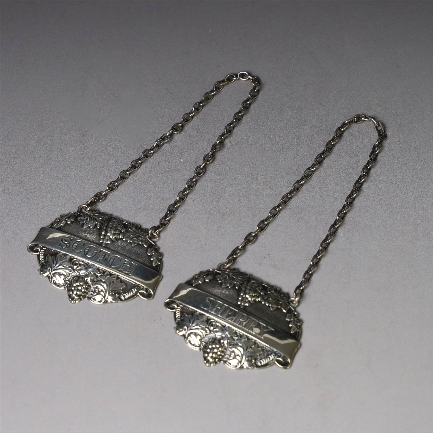 Silver bottle coaster, of circular form with turned wooden centre and pierced sides, hallmarked LGS, London 1977, together with two decanter labels, each with embossed grape vine decoration engraved Scotch and Sherry, hallmarked 