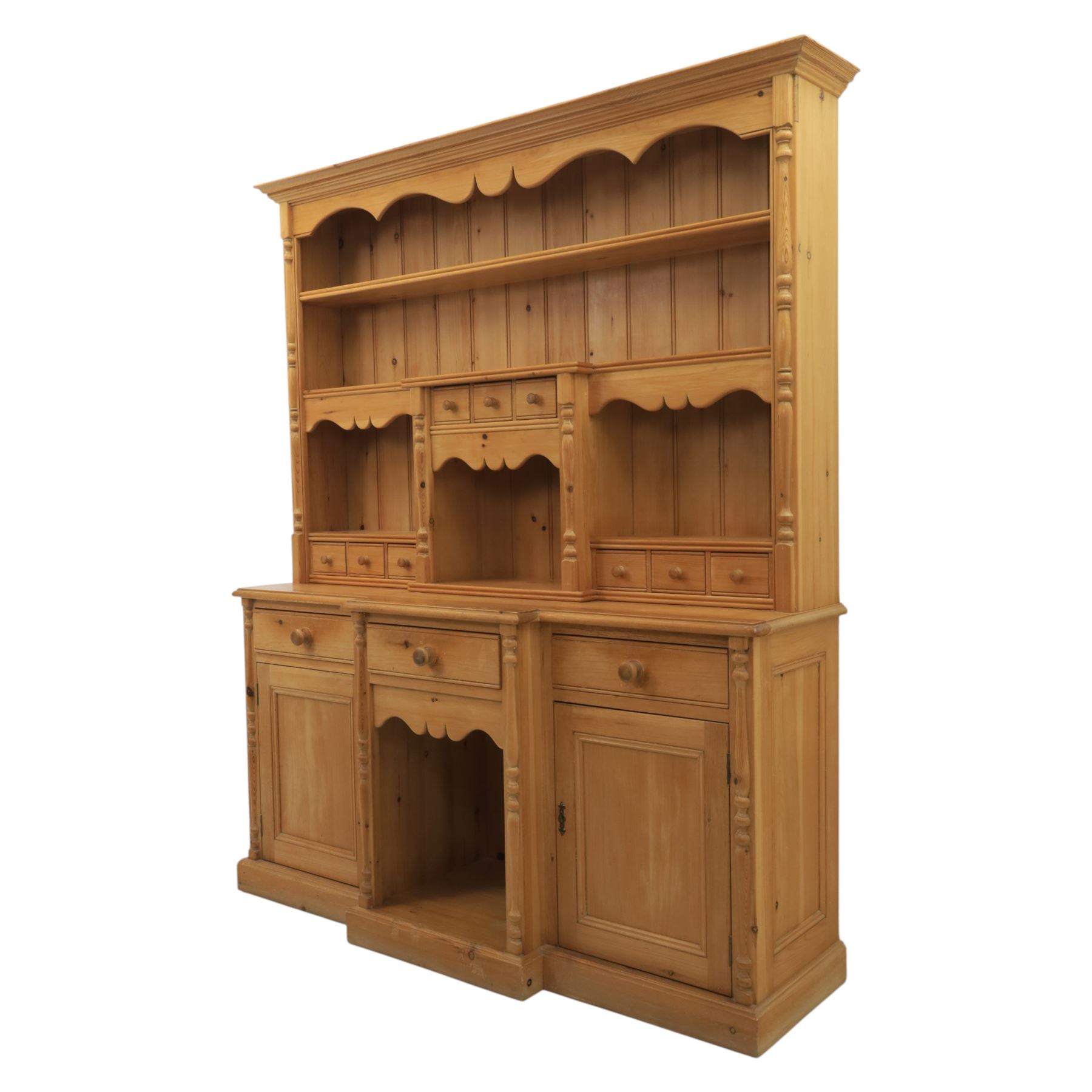 20th century country style waxed pine housekeeper’s cupboard, upper section with moulded cornice, shaped aprons and open shelving around central drawer arrangement, the lower section fitted with three drawers and two cupboards with panelled doors, raised on a plinth base