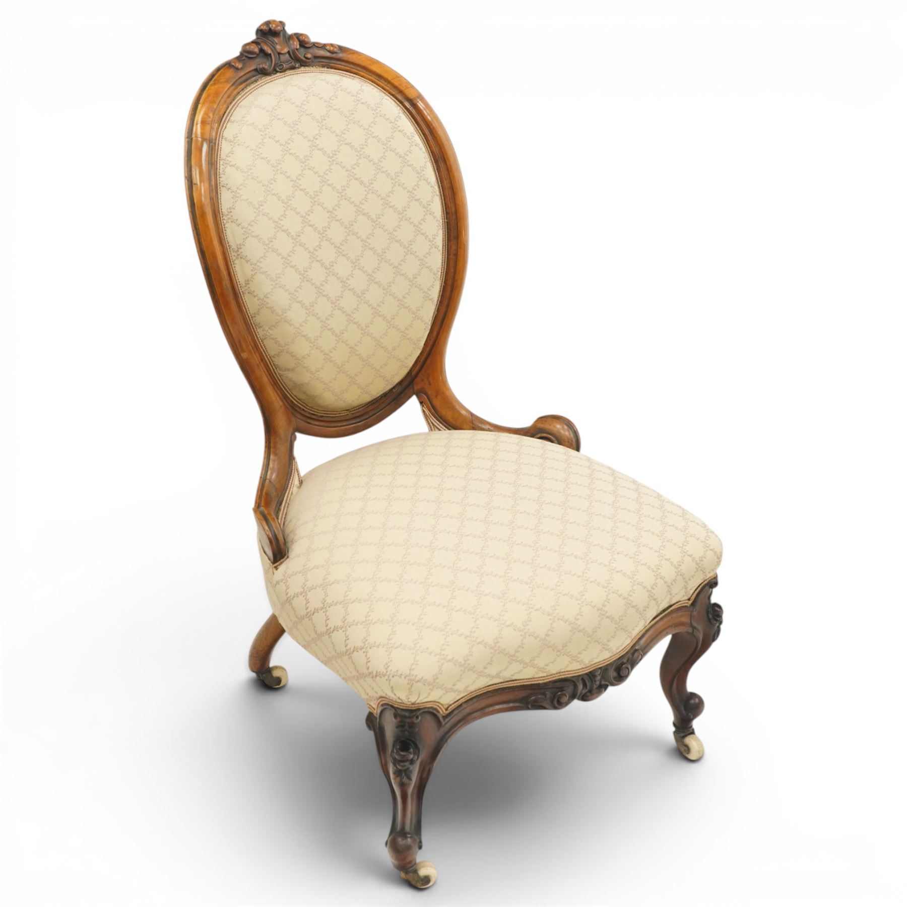Pair of Victorian walnut framed ladies salon nursing chairs, oval cameo back with carved cartouche carved cresting rail, sprung seat upholstered in foliate patterned ivory fabric, shaped apron carved with scroll and cartouche decoration, on cabriole supports with moulded flower knees, retailed by David Hick Interiors, Jersey