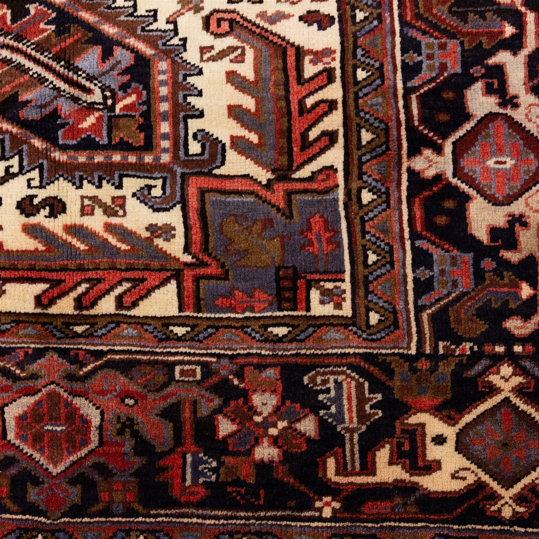 North West Persian Heriz hand-knotted carpet, madder red field with central stepped geometric medallion with radiating angular motifs and serrated outlines, and stylized floral and tribal devices framed by a broad border of repeating angular palmettes and rosettes flanked by multiple guard stripes, with cotton fringe ends 