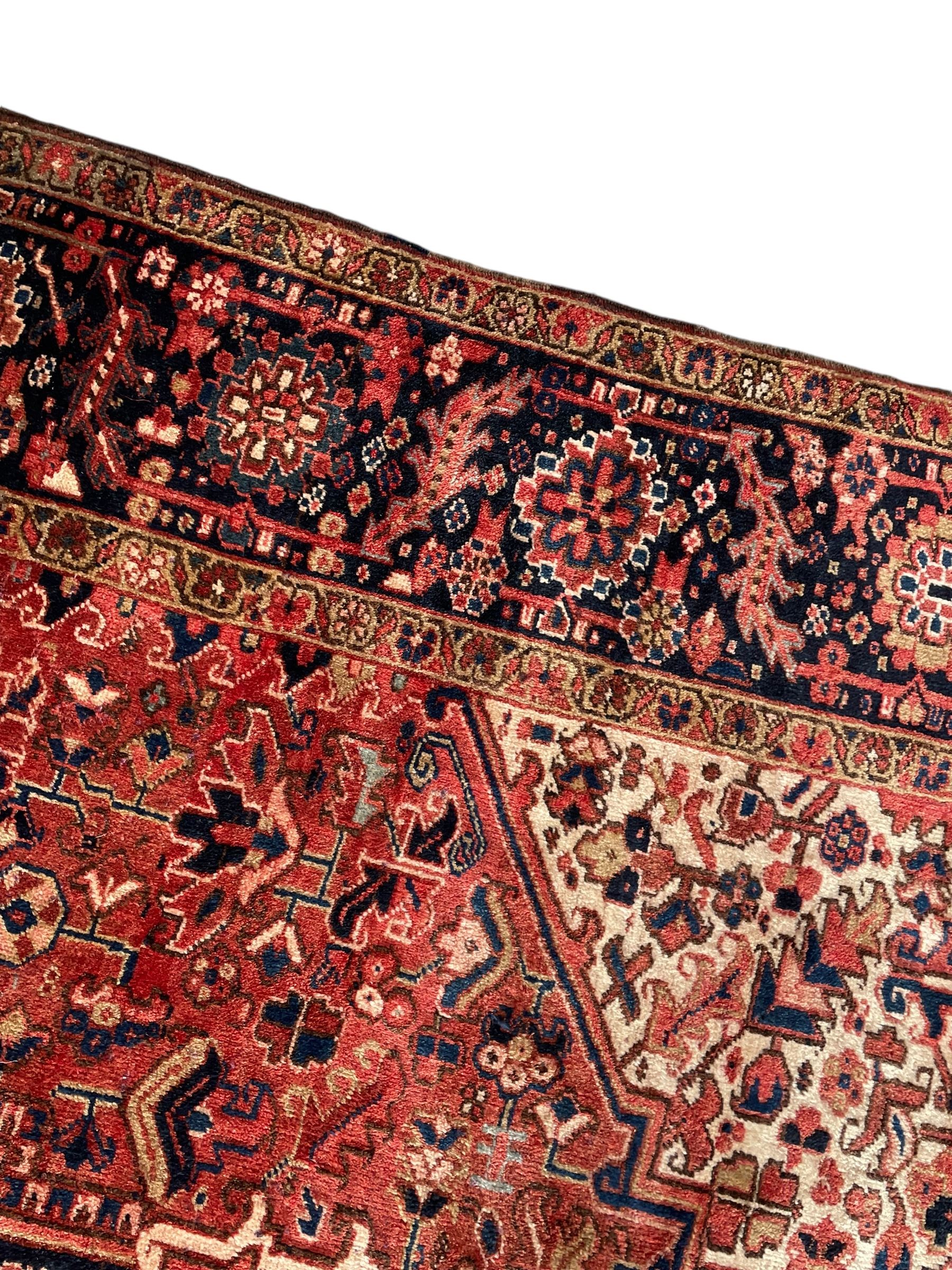 Persian Heriz red ground carpet, large stylised pole medallion surrounded by Pitrak motifs, indigo ground border decorated with stylised flower heads and trailing leafy branches, within floral pattern guard stripes
