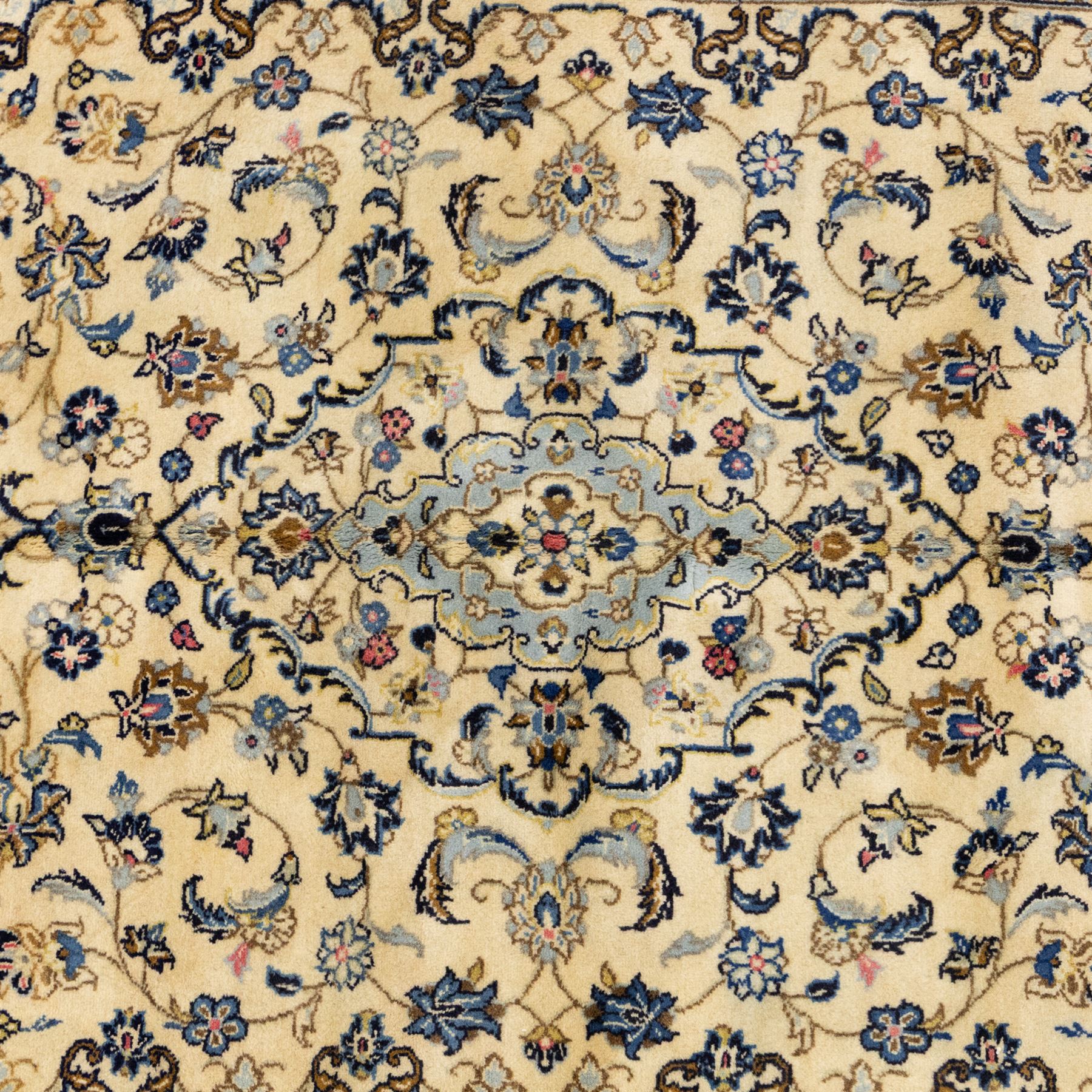 Central Persian Kashan hand-knotted carpet, ivory ground, with a central pale blue shaped floral medallion with pendants, surrounded by scrolling foliate and floral motifs incorporating rosettes, palmettes and delicate vine work in blue, cream and beige tones, enclosed by an ivory border with repeating palmettes and meandering vines, flanked by floral guard stripes, with cotton fringes