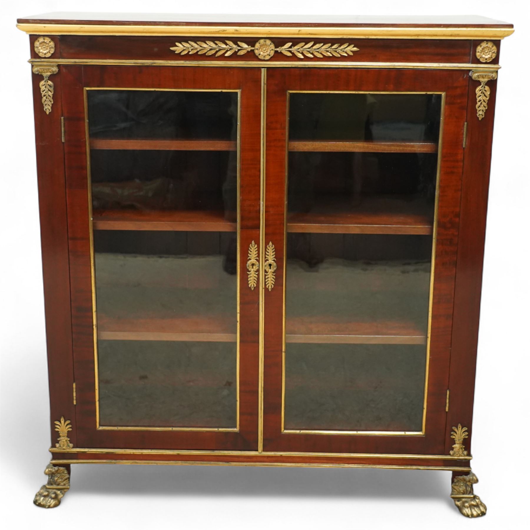 19th-century French Empire-style mahogany and gilt bronze-mounted glazed cabinet, rectangular top above frieze with applied gilt bronze laurel swags and rosettes with gilt brass borders, over two glazed panel doors enclosing three adjustable shelves, flanked by plain pilasters with applied mounts, raised on gilt bronze paw feet 