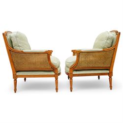 French Empire design varnished wood three piece lounge suite comprising of two cane armchairs and matching sofa, carved top rails with foliate terminals, cane side panels and padded scroll arms, upholstered in a green brocade with matching piping, on fluted legs