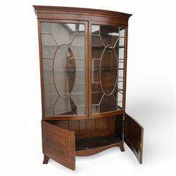 Edwardian mahogany and satinwood bow-fronted display cabinet, moulded dentil cornice over two astragal glazed doors, fitted with three shelves, double cupboard below, the doors inlaid with figured oval panels and satinwood bands, shaped apron on splayed bracket feet 