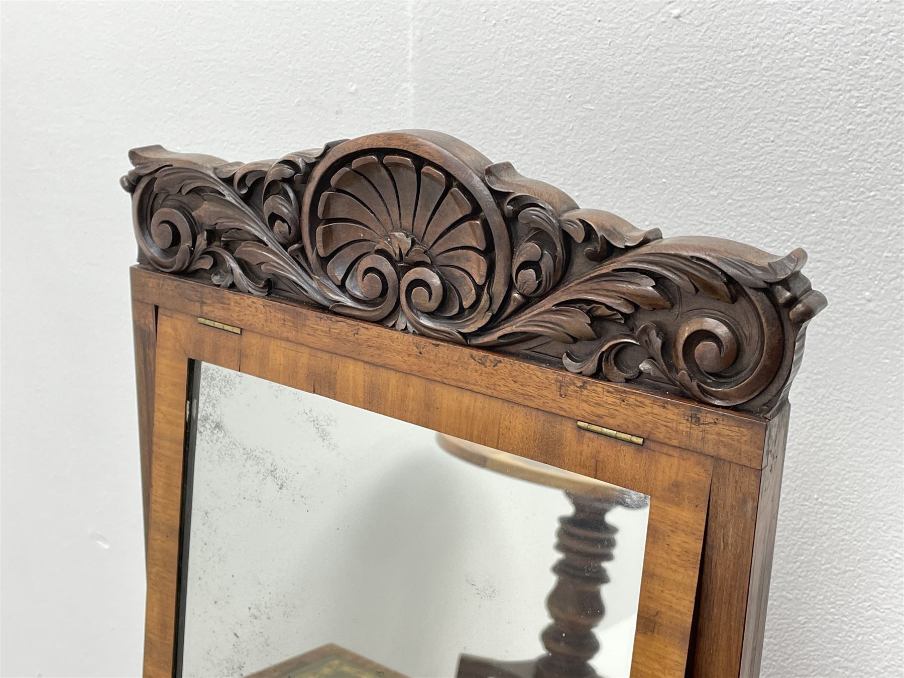 Early Victorian figured mahogany dressing cabinet, the raised shell and scroll carved back lifts to reveal rectangular easel mirror with mahogany band, flat rectangular top with tooled leather inset, slide at each side with matching leather inset, full width drawer above cupboard enclosing a series of five drawers, turned front supports, panelled front, sides and back