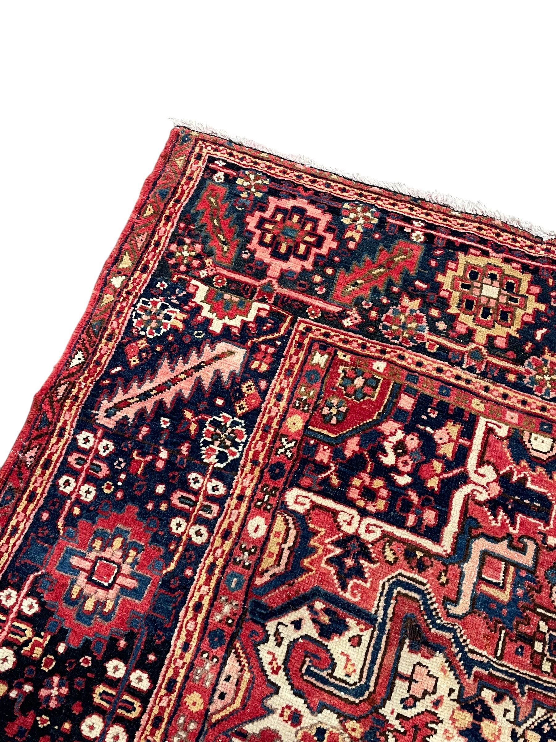 Persian Heriz crimson ground carpet, large central medallion comprising projecting palmettes with surrounding stylised plant motifs and trailing branches, the main border decorated with stylised leaf and flower head motifs within geometric pattern guard stripes