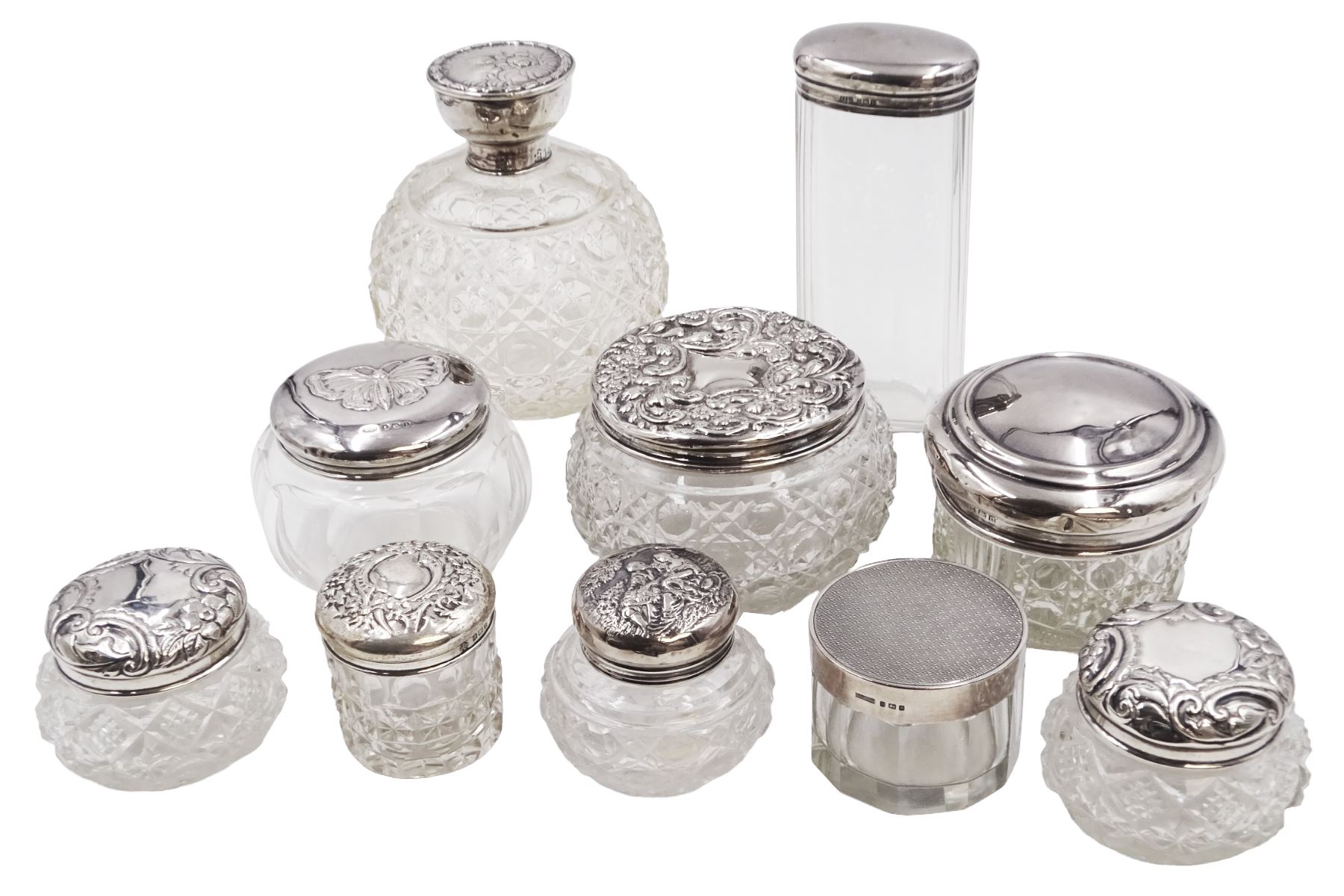 Mid 20th century silver topped cut glass scent bottle, with hobnail and octagonal decoration to the glass body, the silver lid repousse decorated with putti, hallmarked Boots Pure Drug Company, Birmingham 1943, together with nine silver topped glass dressing table jars, with designs including butterfly and romantic scene,  all with hallmarked with various makers and dates