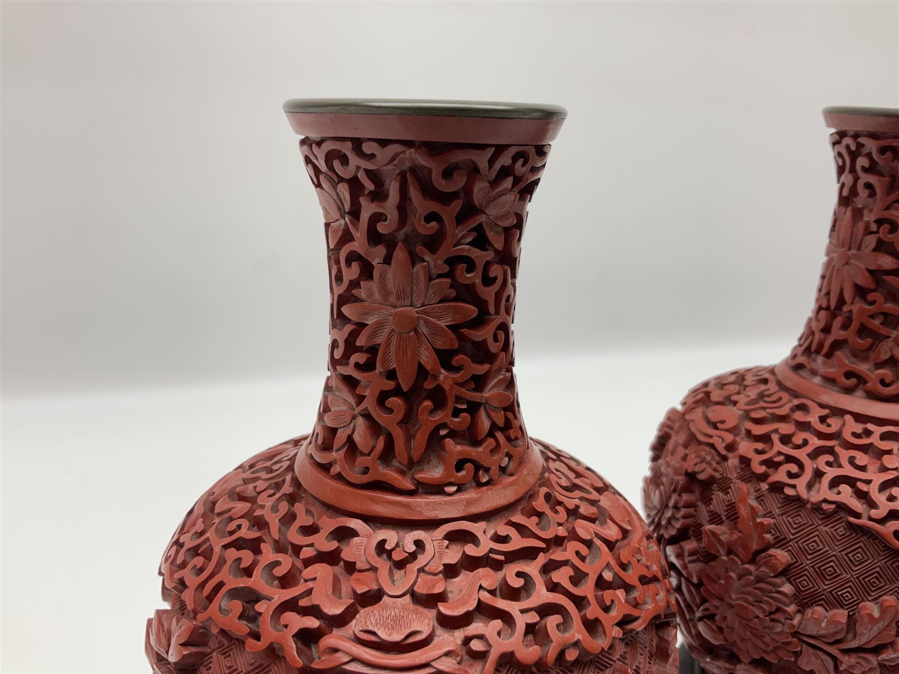Pair of Chinese cinnabar lacquer vases, each of bulbous baluster form, carved with peonies and foo dogs amongst scrolls, with blue enamel interior and upon wooden bases, H20cm