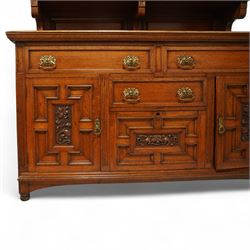 Early 20th century golden oak dresser sideboard, superstructure with three stained and leaded glass doors flanked by carved uprights above an open display shelf, the base with three drawers and geometric panelled cupboard doors, enclosing drawers with cutlery and bottle compartments, raised on short feet