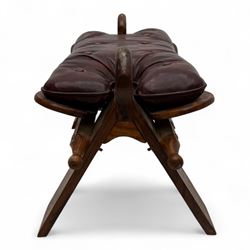 Pair of early 20th century Anglo-Indian camel saddle stools, with deep buttoned red leather upholstered seats and horn-shaped pommels, on X-form supports with turned ball finials