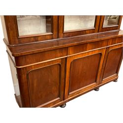 Large Victorian mahogany bookcase on cupboard, projecting cornice over three glazed doors enclosing lined shelves and back, the lower section fitted with three drawers and three panelled cupboards, plinth base on turned feet 