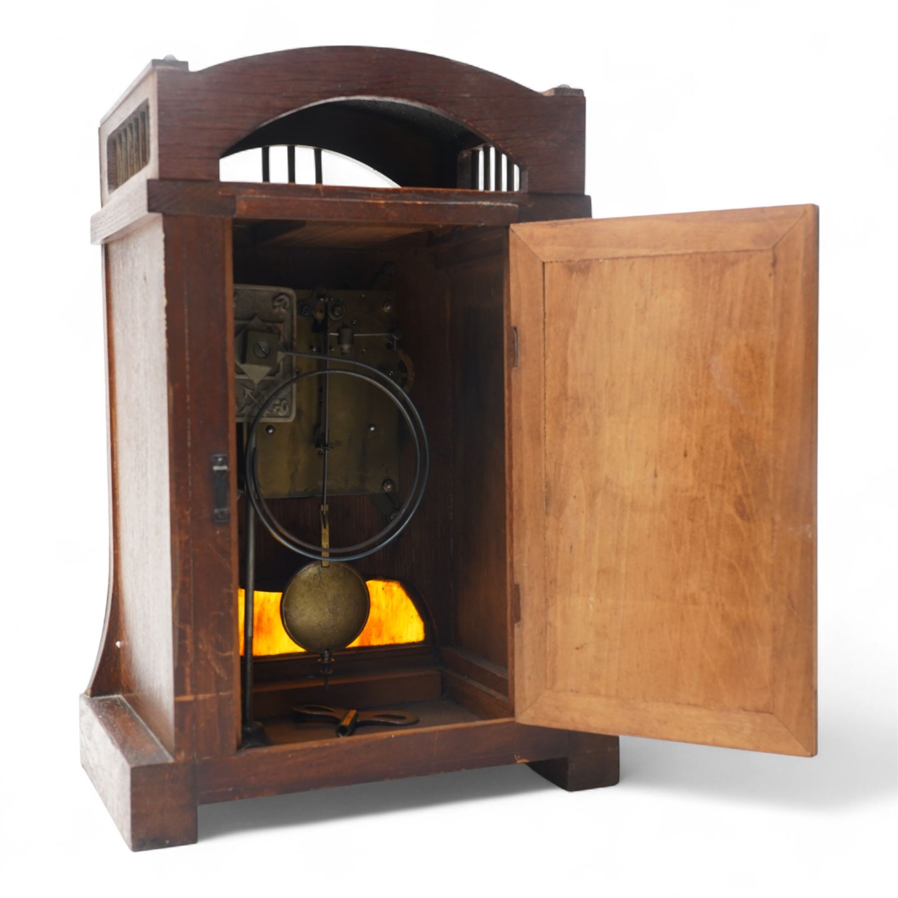Early 20th century-German Arts & Crafts oak cased mantel clock with a two train movement by the Hamburg and American Clock Company, case with a rounded pediment and gallery to the front and sides, formerly silvered dial and brass strapwork to the front with a multi-coloured glass panel beneath, conforming hammered dial with Arabic numerals and contrasting steel serpentine hands, twin train countwheel striking movement, striking the hours and half hours on a coiled gong.
With pendulum and key.