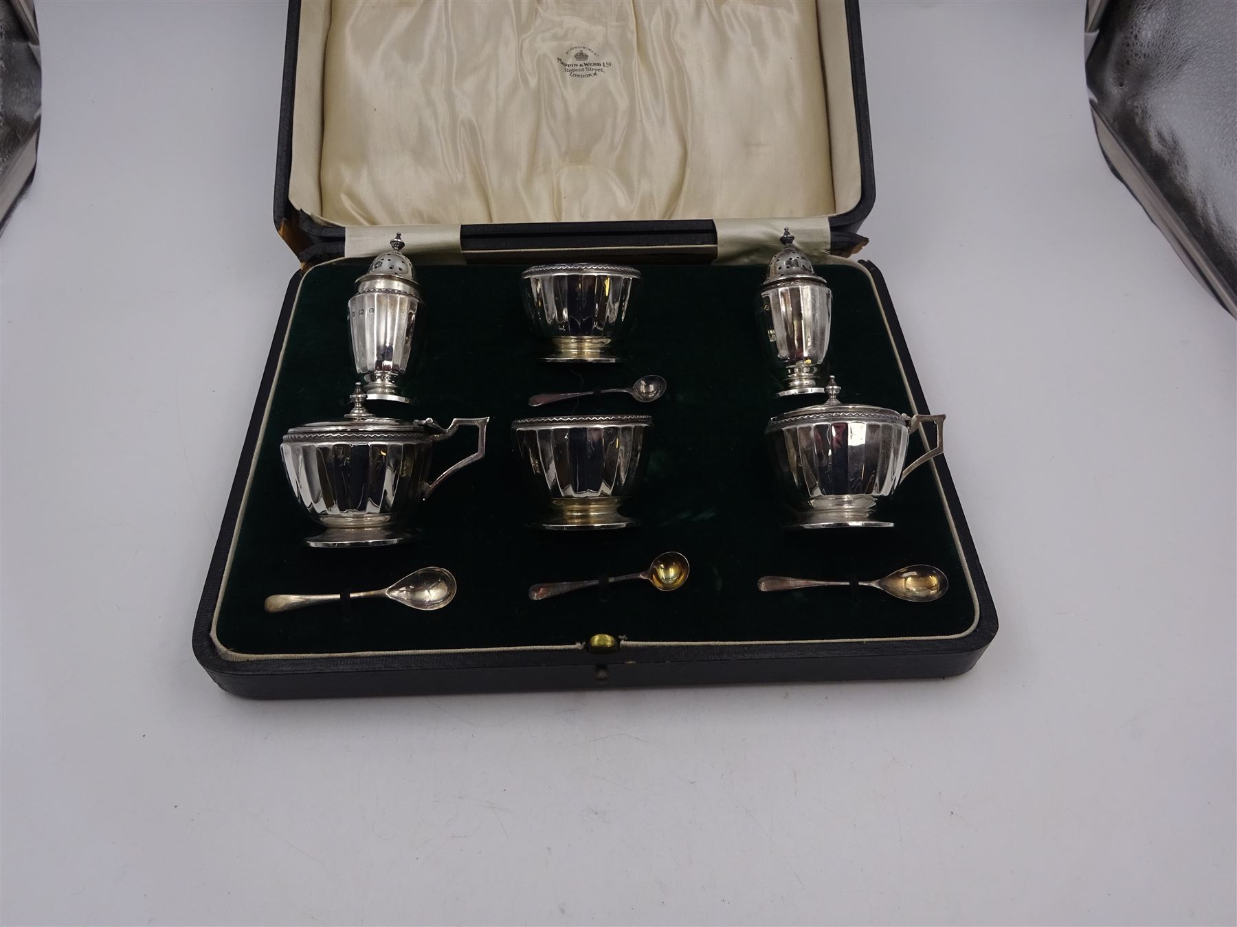 1920s silver six piece cruet set, comprising two mustard pots with covers, two open salts and two pepper pots, all of circular faceted form, mustards and salts with blue glass liners, hallmarked Mappin & Webb, Birmingham 1928, with four matched silver condiment spoons, hallmarked, contained within fitted case 