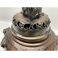 Japanese bronzed koro, the body of globular form with twin cast zoomorphic mask handles, decorated in relief with birds upon blossoming branches, against a ground incised with rushes and peonies, the flat toped domed cover with pierced band and surmounted by a cast figure of a Foo dog, the whole upon three zoomorphic mask feet, with impressed character type mark beneath, H35.5cm