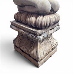 20th century composite stone garden figure, modelled as a kneeling nude female with arms raised behind her head, mounted on an integral cushion, the squared ogee pedestal moulded with acanthus leaves and flower heads, in a white painted and weathered finish